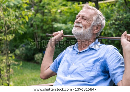 Thoughtful depressed senior old caucasian man holding cane with two hands sitting in garden
