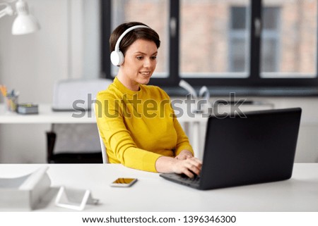 business, technology and people concept - happy creative woman in headphones with laptop computer working and listening to music at office