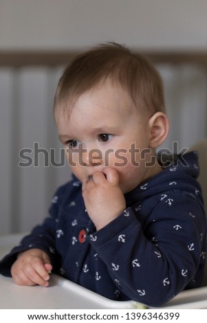 Medium vertical shot of adorable fair toddler girl with dreamy expression eating finger food in high chair