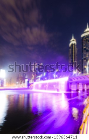 (Defocused) Blurred picture of the illuminated Dubai skyline with the beautiful colored waterfalls seen from the Dubai Water Canal boardwalk. Dubai, United Arab Emirates.