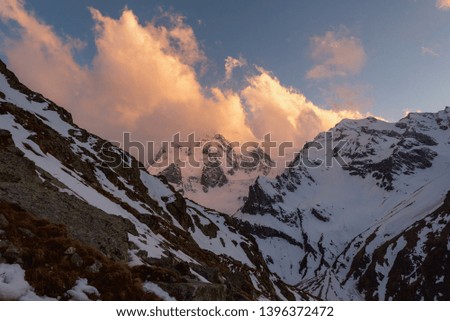 mountain peaks covered with snow with bright clouds in the evening at sunset against the blue sky. Kabardino-Balkaria, Russia