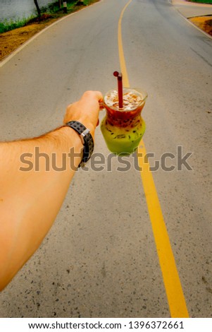 Male hand holding beautiful drink on middle of the road with vertical yellow dividing line Jar of iced Matcha green tea and coffee in layers