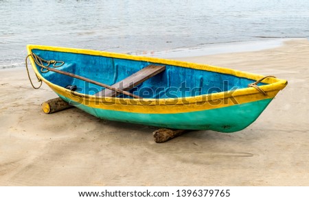 Beautiful photo of beached Fishing Canoe, the canoe is painted colorful in traditional asian manner. It is idle in off season parked on wooden logs, due to rough weather forecast of cyclone. - Image