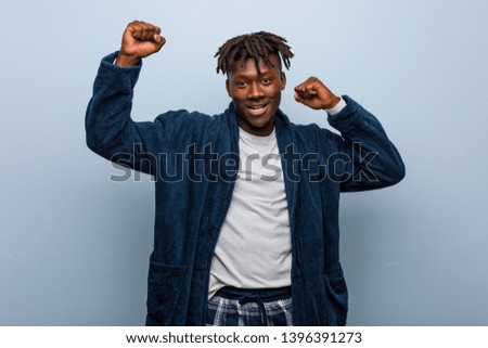 Young african black man wearing pajama celebrating a special day, jumps and raising arms with energy.