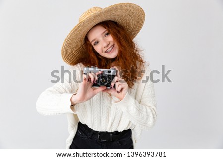 Close up portrait of a cheerful young teenage girl wearing summer hat standing isolated over white background, holding photo camera