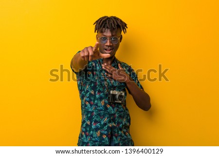 Young black rasta man wearing a vacation look points with thumb finger away, laughing and carefree.