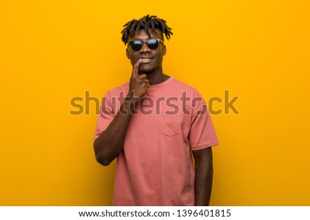 Young casual black man wearing sunglasses looking sideways with doubtful and skeptical expression.