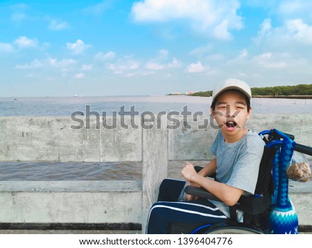 Child on wheelchair waiting to see seagull, He held the bird's food in his hand and excited on the bridge background, Life in the education age of disabled children, Happy disabled kid concept.