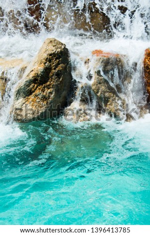 Waterfall flowing over rocks in various colors and deep blue water below