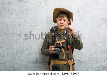 Young chinese explorer man holding a camera showing number one