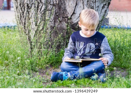 Boy is reading a book in a park. Fall, daylight. 