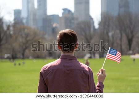 Young man with an American flag in Central Park in New York City in spring. 