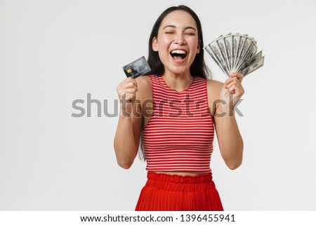 Photo of a beautiful young pretty asian excited woman posing isolated over white wall background holding credit card and money.