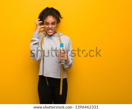 Young fitness black woman angry and upset.Holding a water bottle.