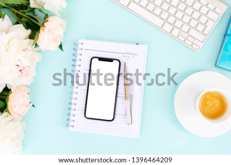 Home office desk with peony flowers, white keyboard and modern phone mock up on blue background