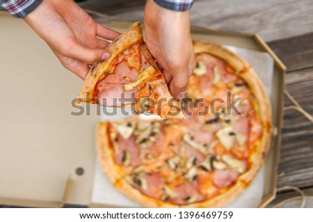 Boy hand holding a slice of delicous pizza, eating pizza in a park 
