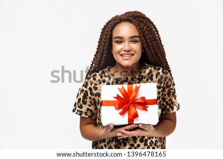 Image of cheerful african american woman smiling and holding present box with bow while standing isolated against white background