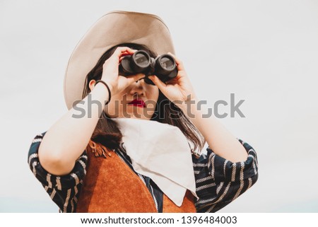 cute chinese cowgirl while looking at the horizon with binoculars on a wild west farm