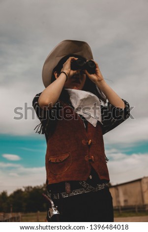 cute chinese cowgirl while looking at the horizon with binoculars on a wild west farm