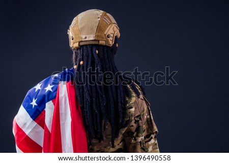afro american army latin soldier in camouflage clothes hair dreadlocks evening makeup and big lips on a black background in the studio with american flag back view