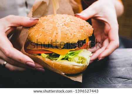 Female hands holding fresh delicious burger with french fries on the black wooden table