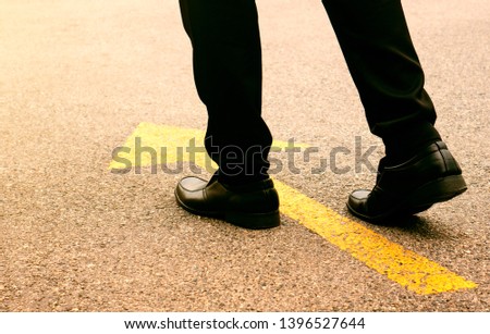 Concept of moving forward: Black leather shoes on a tarmac road with yellow direction arrow. Royalty-Free Stock Photo #1396527644