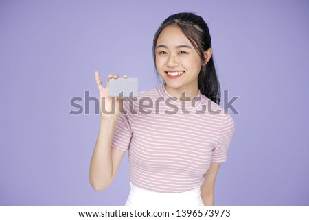 Asian young teenage beautiful cheerful girl hold membership or credit card in pink shirt, on violet background