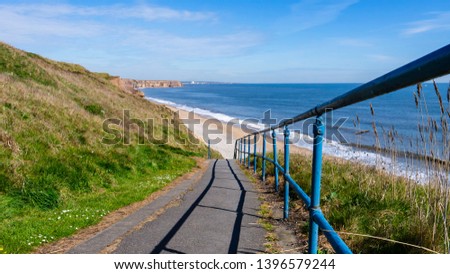 Stairway down to Seaham Hall Beach in County Durham, England UK.  Image taken on a warm sunny day showing blue sea, golden sand and blue sky. Royalty-Free Stock Photo #1396579244