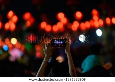 Focusing on unidentified woman is lifting the mobile phone to take a photo of celebrations at night.