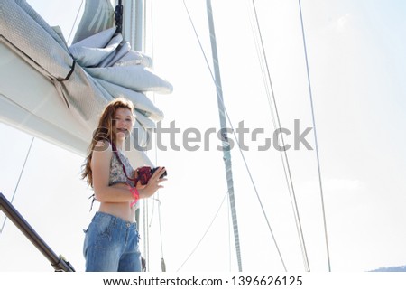 Beautiful teenager girl holding photographic camera on luxury private sailing yacht on summer holiday, looking smiling outdoors. Fun day out activities, aspirational leisure recreation lifestyle.