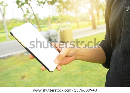 Asia man using and holding a smartphone device for working or chatting while in the park outdoor, hand holding mockup phone