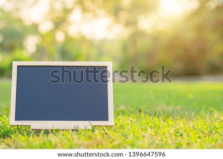 empty wooden blackboard in square shape on green grass in the park background.