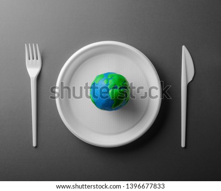 Serving table with colored Earth planet and black and white plastic plate, fork and knife. Ecology Concept for Earth Hour, Earth Day, Ocean Day and other ECO dates.