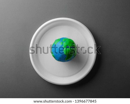 Black and white serving table with colored Earth planet on plastic plate. Ecology Concept for Earth Hour, Earth Day, Ocean Day and other ECO dates.