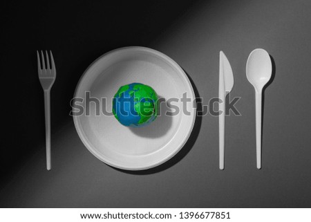 Serving table with colored Earth planet and black and white plastic plate, spoon, fork and knife. Ecology Concept for Earth Hour, Earth Day, Ocean Day and other ECO dates.