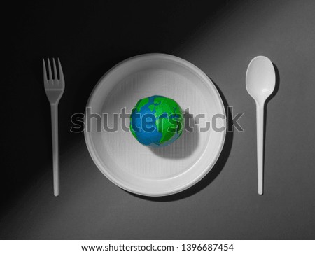 Serving table with colored Earth planet and black and white plastic plate, spoon and fork. Ecology Concept for Earth Hour, Earth Day, Ocean Day and other ECO dates.