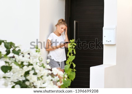  Beautiful woman opening the door of her home,typing text message.Using smart phone.