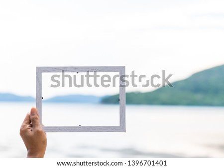 A  hand  of  woman  holding white wooden  picture  frame  with  nature   blurry  background