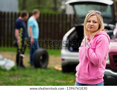 portrait of a caucasian woman on the background of a car in which two men change the wheel