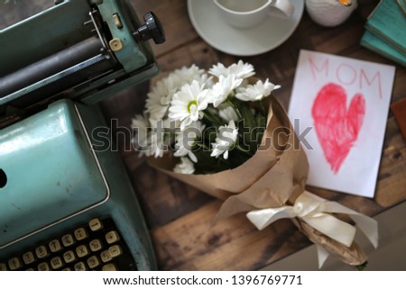 a bouquet of flowers in Kraft paper and a card with a heart and mom on a wooden table, a bouquet of chrysanthemums for mom, craft style and toning. Mother's Day Concept and Greetings
