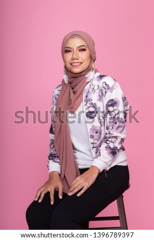 Fashionable young woman in white top, long sleeves jacket and hijab isolated on pink background. Stylish Muslim female hijab fashion lifestyle portraiture concept.