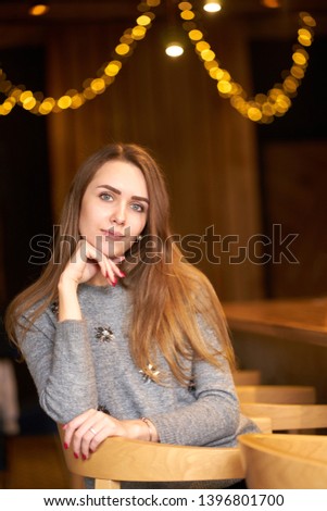 Portrait of young attractive smiling frendly woman with long hair wearing grey sweater. Indoors.                                