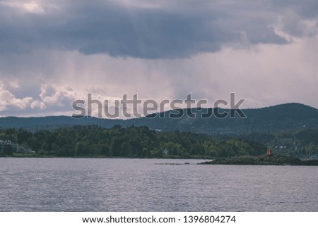rocky coastline in Norway with few pine trees and calm water under blue sky - vintage retro look