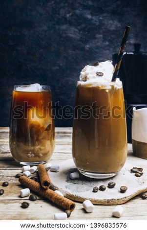 Ice coffee in a tall glass with cream poured over and coffee beans Greek drink frappe with milk. Cold summer drink on a dark wooden background. Selective focus