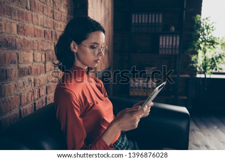 Profile side view photo serious concentrated assistant hold hand device search information do analysis sit sofa eyeglass trendy style stylish red sweater skirt brunette beautiful industrial free time