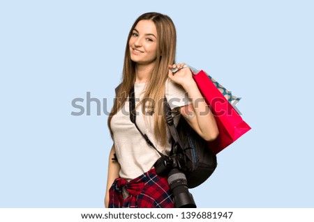 Young photographer woman holding a lot of shopping bags on isolated blue background