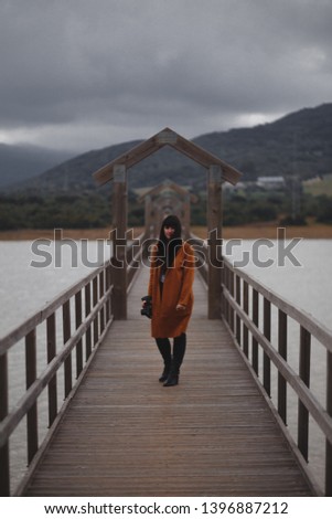 Brunette woman photographer with orange trench coat on a bridge