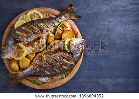 Roasted fish and potatoes, served on wooden tray. overhead, horizontal, copy space - image Royalty-Free Stock Photo #1396894352