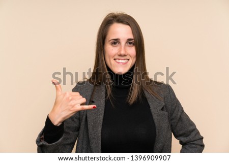 Young woman over isolated wall making phone gesture