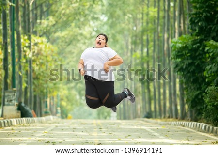 Picture of an excited fat woman leaping on the road while wearing sportswear